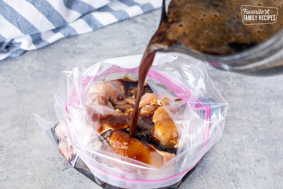 Pouring teriyaki marinade into an open ziplock bag with chicken thighs.