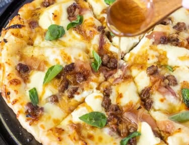 Drizzling hot honey on top of a baked hot honey pizza with fresh basil leaves.
