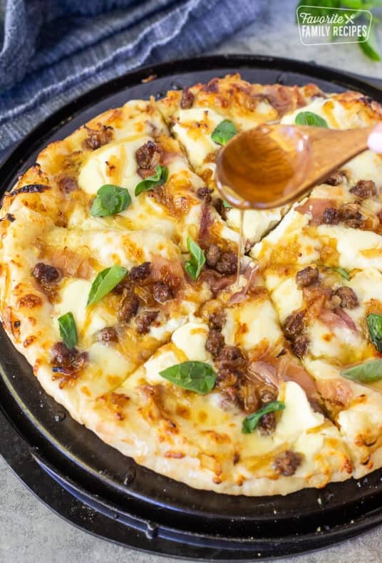 Drizzling hot honey on top of a baked hot honey pizza with fresh basil leaves.