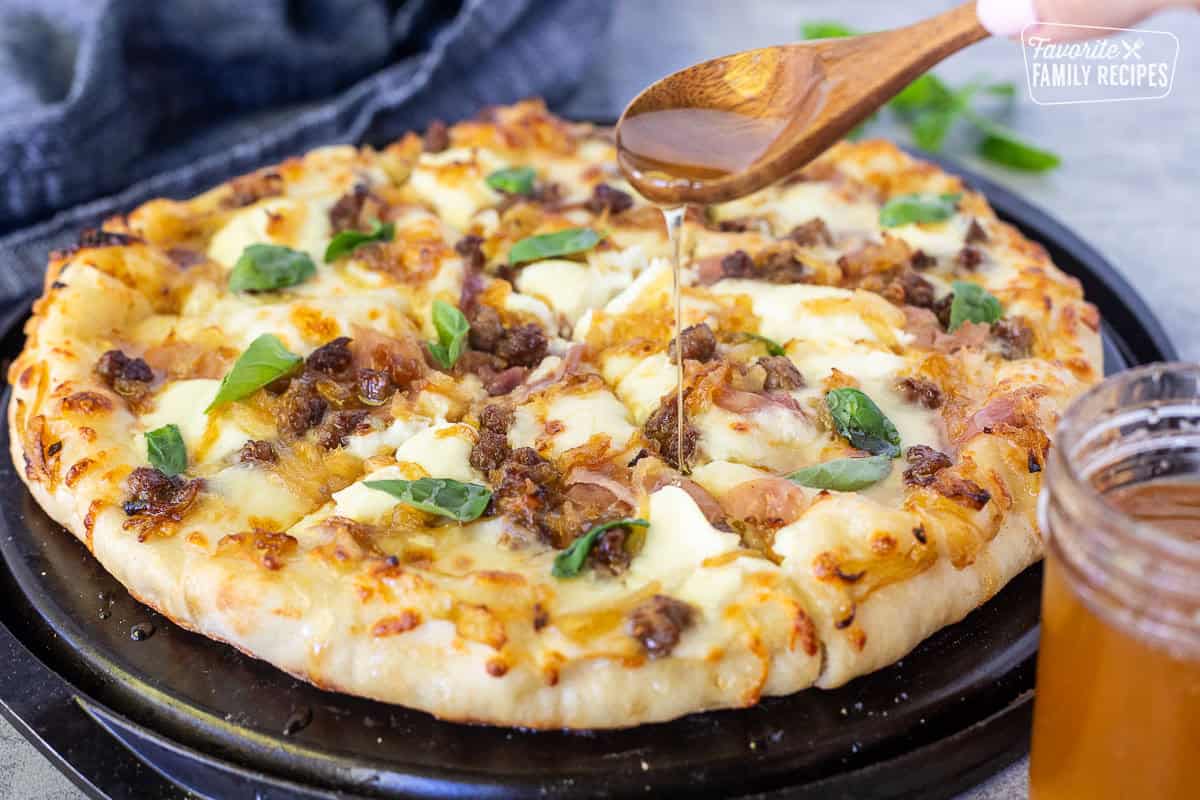 Drizzling hot honey on top of a baked hot honey pizza with fresh basil leaves.