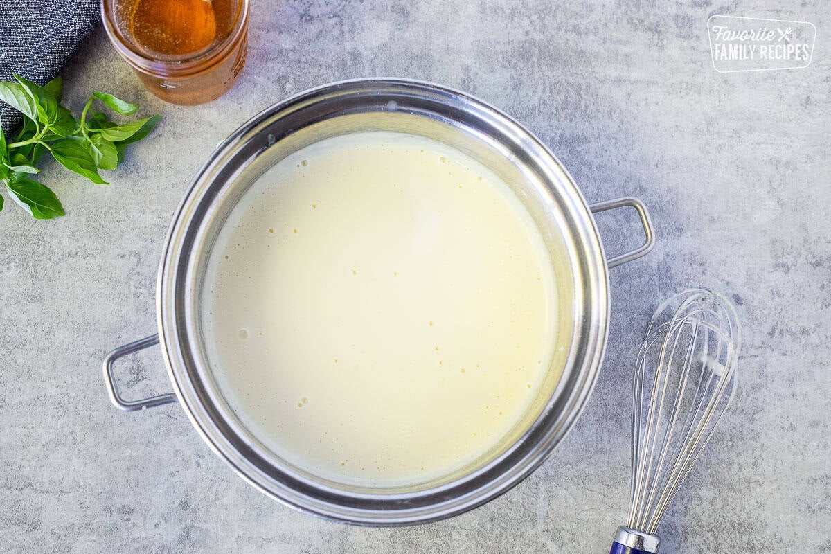 Saucepan with white Alfredo sauce and a whisk on the side.