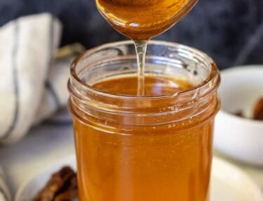 Hot honey in a glass jar with a wooden spoon lifted about and the honey drizzling into the jar. Habanero peppers on the sides.