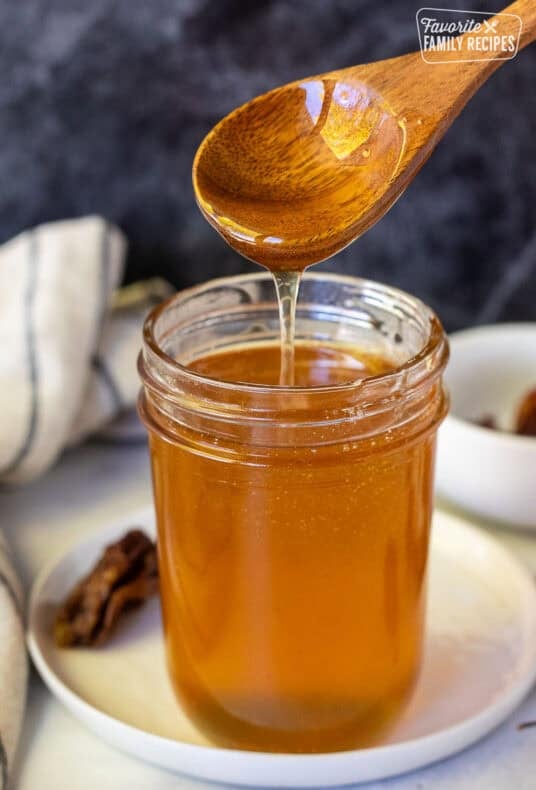 Hot honey in a glass jar with a wooden spoon lifted about and the honey drizzling into the jar. Habanero peppers on the sides.