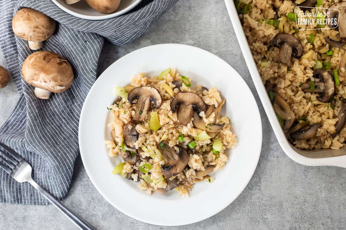 Casserole dish and plate with Mushroom Rice with sliced mushrooms, cut celery, slivered almonds and sliced green onion.
