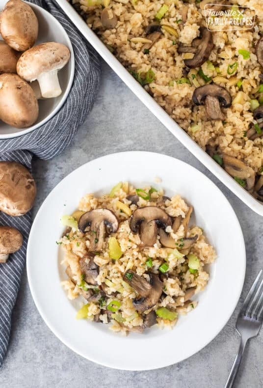 Casserole dish and plate of baked Mushroom Rice with sliced mushrooms, cut celery, slivered almonds and sliced green onion.