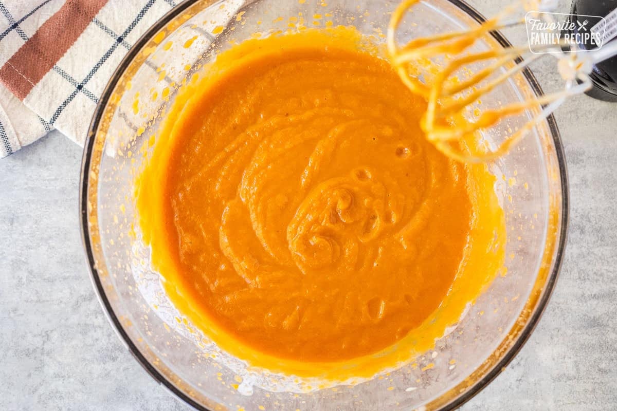 Glass mixing bowl with pumpkin mixture and electric mixer on the side.
