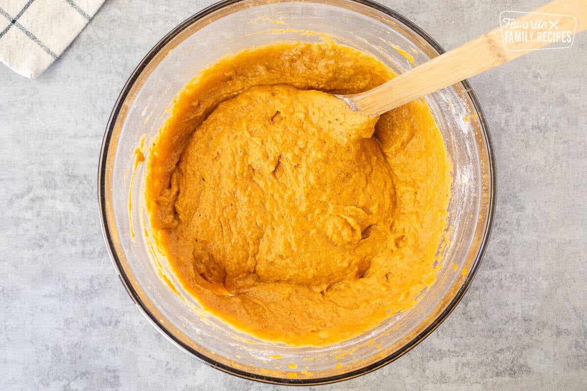 Pumpkin bread batter in a glass mixing bowl with a wooden spoon.