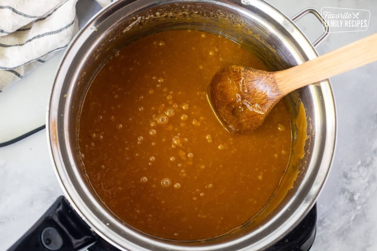 Saucepan with butter combined in hot caramel mixture and a wooden spoon.
