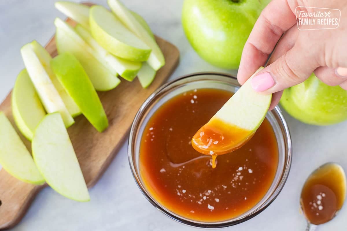 Dipping a green apple slice into a bowl of salted caramel sauce.