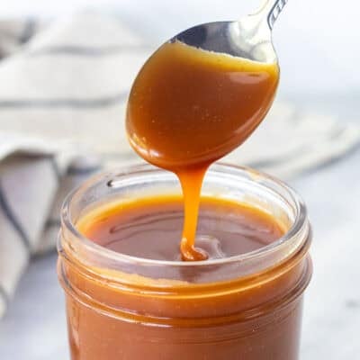 Drizzling salted caramel sauce from a spoon into a jar.