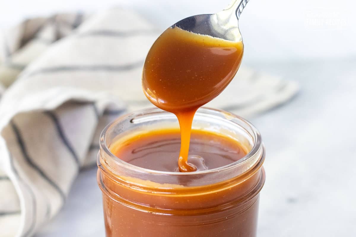 Drizzling salted caramel sauce from a spoon into a jar.