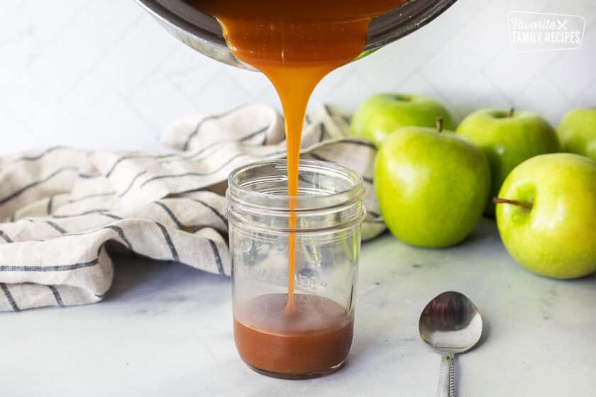Pouring salted caramel sauce from a saucepan into a glass jar. Green apples in the background.