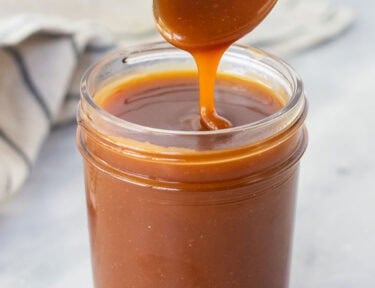Drizzling salted caramel sauce from a spoon into a jar.