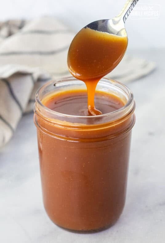 Drizzling salted caramel sauce from a spoon into a jar.