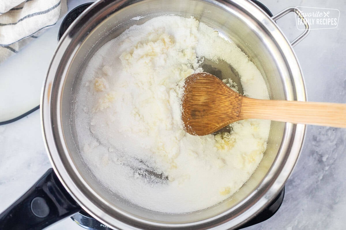 Saucepan with sugar starting to clump and a wooden spoon.