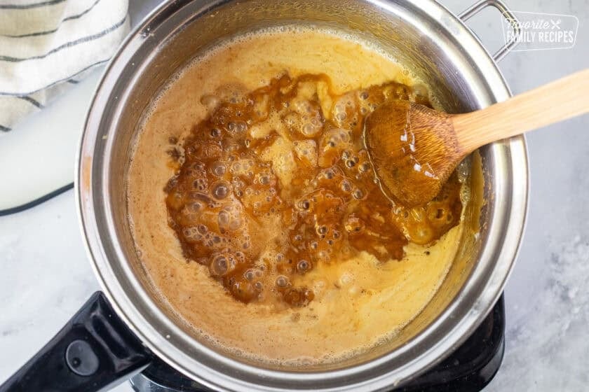 Saucepan with heavy cream poured into hot caramel mixture and a wooden spoon.