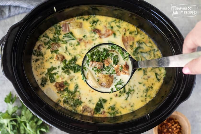 Ladle coming out of a crockpot with a serving of Zuppa Toscana soup.