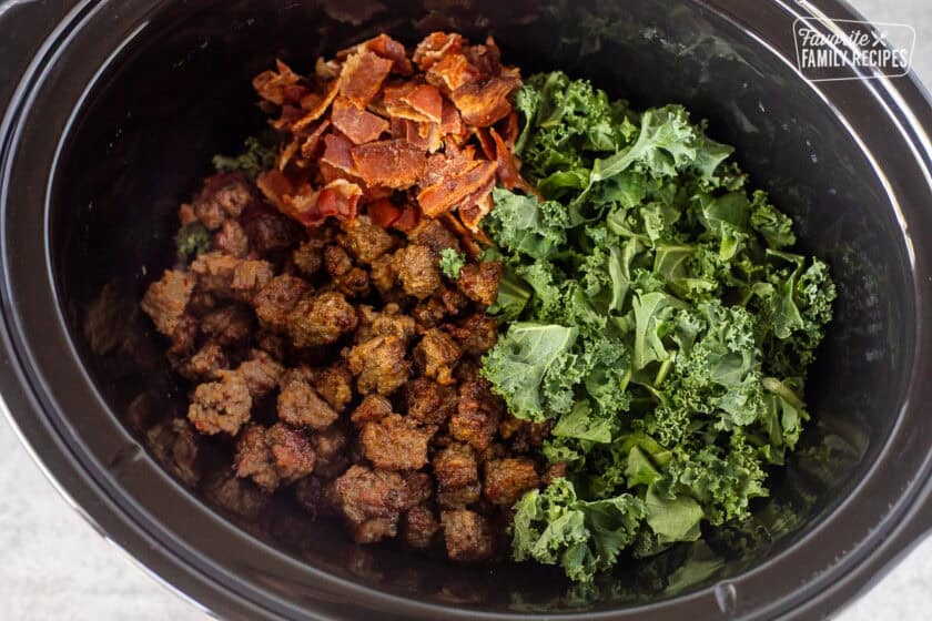 Crockpot with kale, bacon pieces and sausage pieces.
