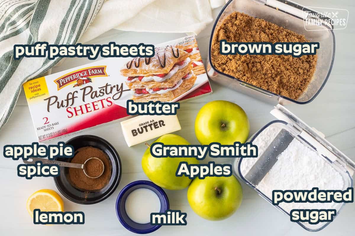 Ingredients to make Apple Turnovers including puff pastry sheets, butter, brown sugar, powdered sugar, green apples, apple pie spice, milk and lemon juice.