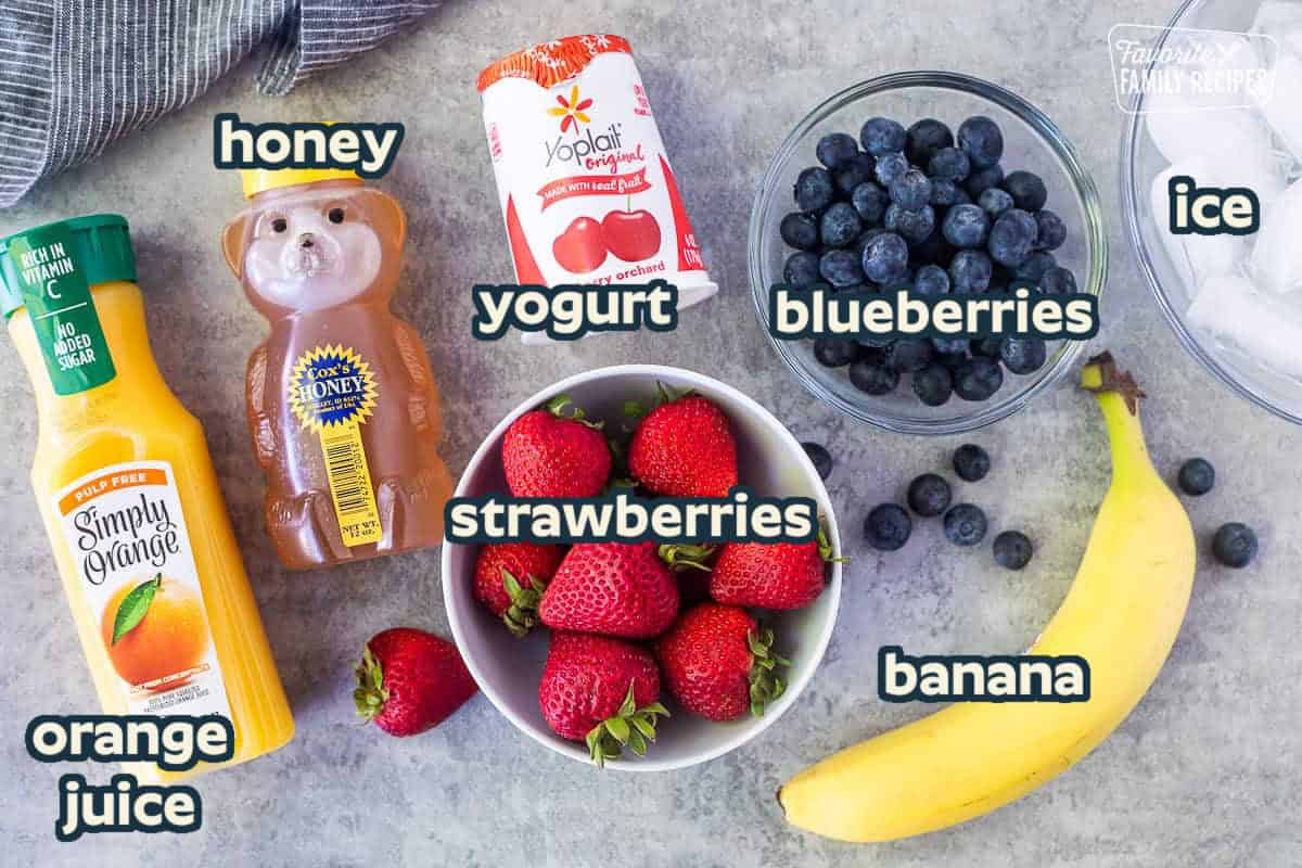 Ingredients to make a banana berry smoothie including blueberries, banana, ice cubes, strawberries, cherry yogurt, honey and orange juice.