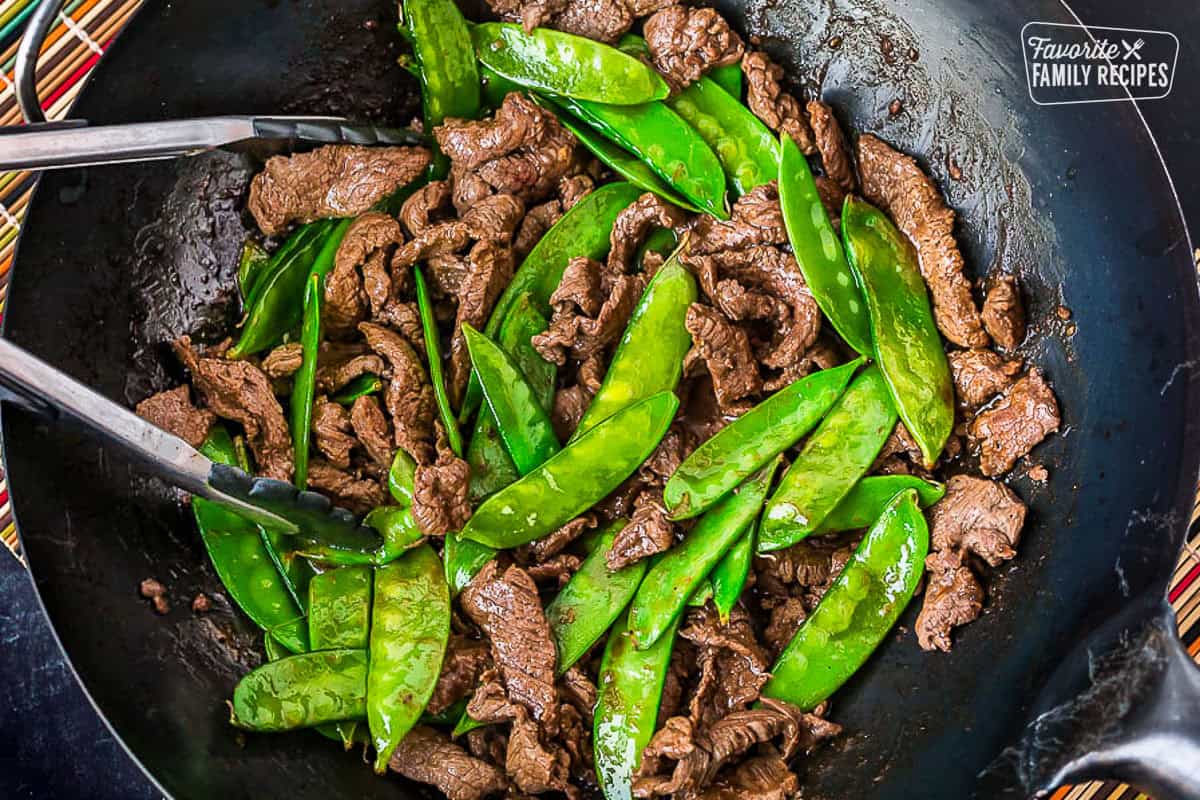 Beef and snow peas with tongs cooked and a hot wok skillet.