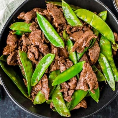 Beef and snow peas in a bowl next to a bowl of rice and chopsticks.