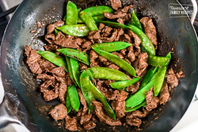 Adding snow peas into a walk of seared beef pieces.