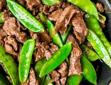 Beef and snow peas in a bowl with rice and chopsticks on the side.