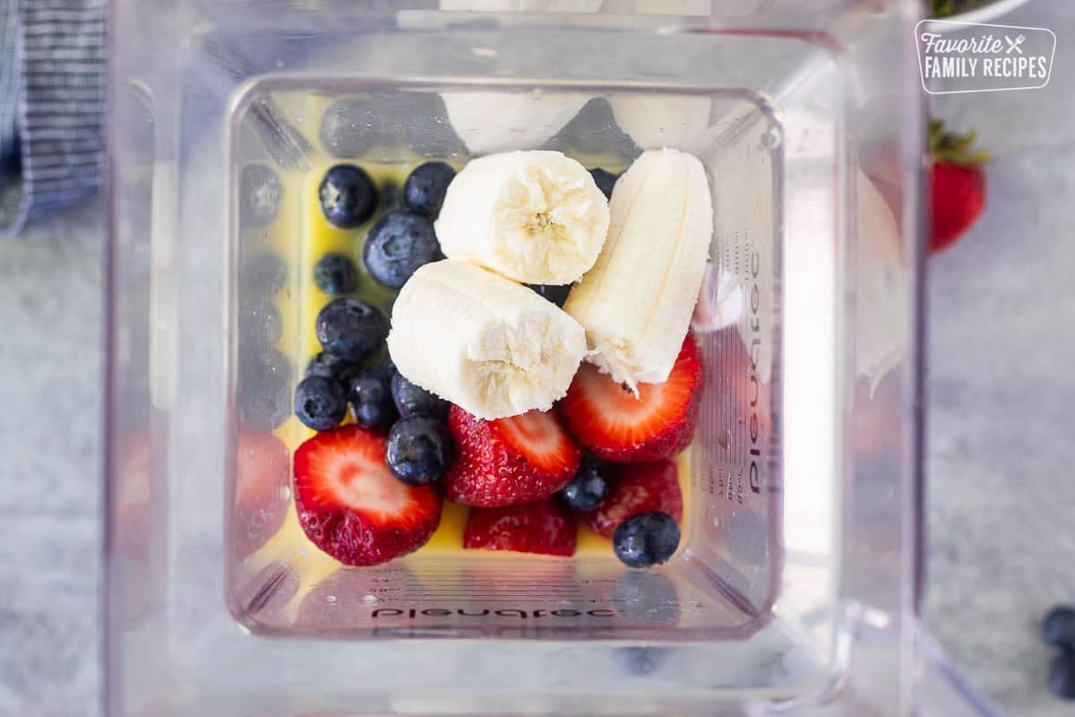 Blender with orange juice, yogurt, bananas, strawberries and blueberries.