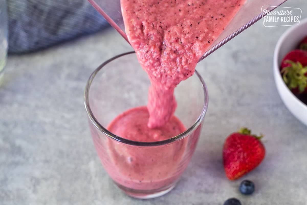 Pouring berry banana smoothie from a blender into a glass.