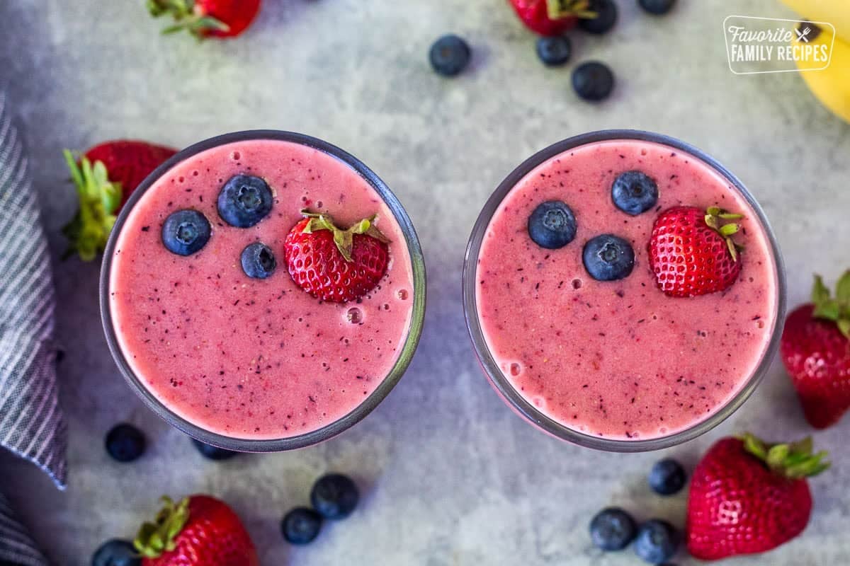 Two glasses of berry banana smoothie garnished with a fresh strawberry and three blueberries on top.