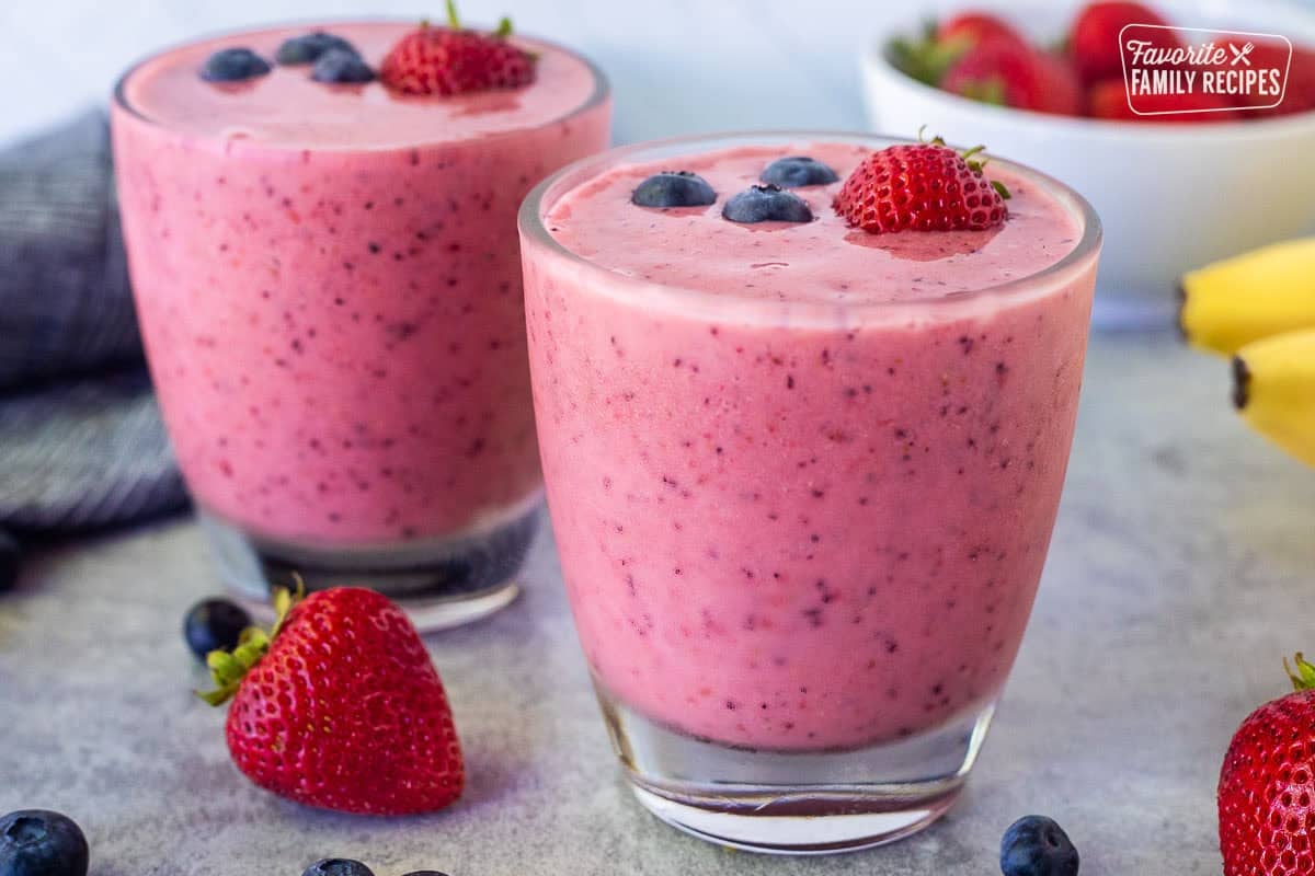 Glasses with berry banana smoothie garnished with a fresh strawberry and three blueberries on top.