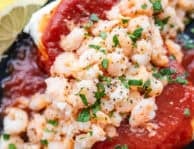 Close-up of cream cheese shrimp dip with a brick of cream cheese, cocktail sauce, tiny shrimp and garnished with lemon wedges and parsley.