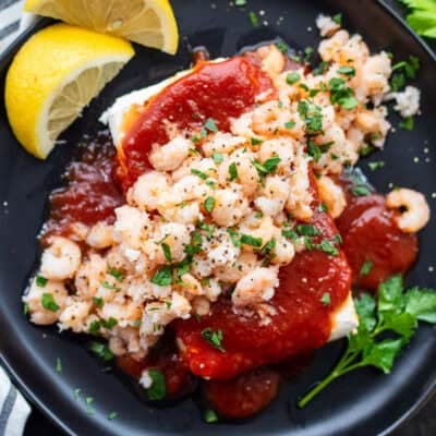 Plate with cream cheese shrimp dip consisting of cream cheese, cocktail sauce, tiny shrimp and garnished with parsley. Crackers on the side.