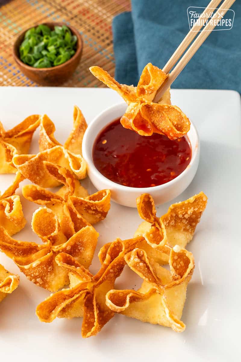Using chopsticks to dip a cream cheese wonton into sweet-and-sour sauce.