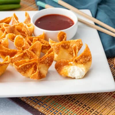 Cream cheese wontons on a platter next to a bowl of sweet-and-sour sauce. Cut open cream cheese wonton.