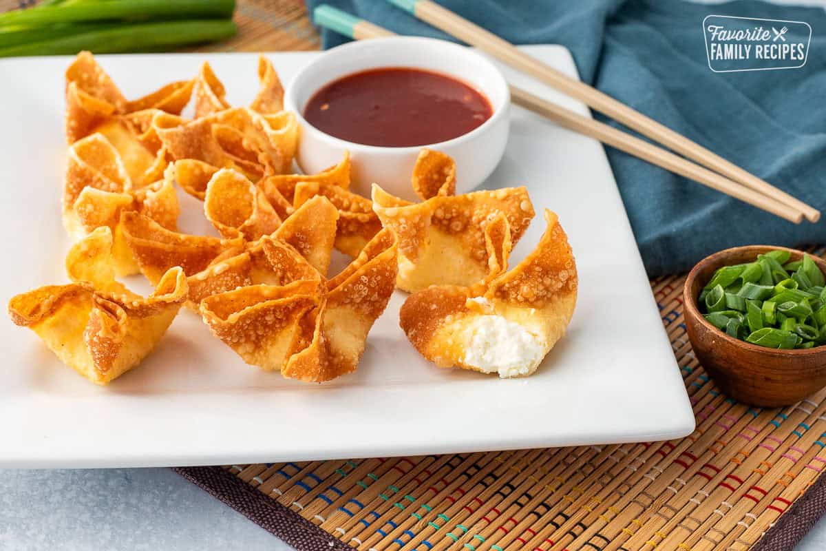 Cream cheese wontons on a platter next to a bowl of sweet-and-sour sauce. Cut open cream cheese wonton.