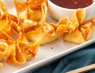Cream cheese wontons on a plate next to a small bowl of sweet-and-sour sauce.