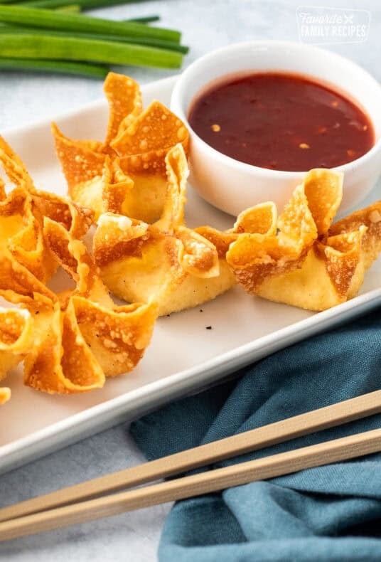 Cream cheese wontons on a plate next to a small bowl of sweet-and-sour sauce.