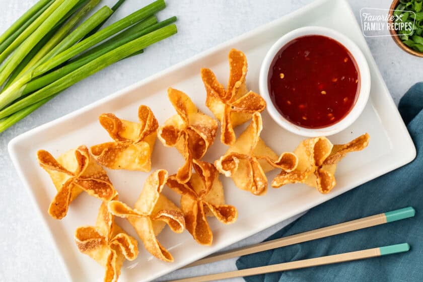 Cream cheese wontons on a platter next to a bowl of sweet-and-sour sauce.