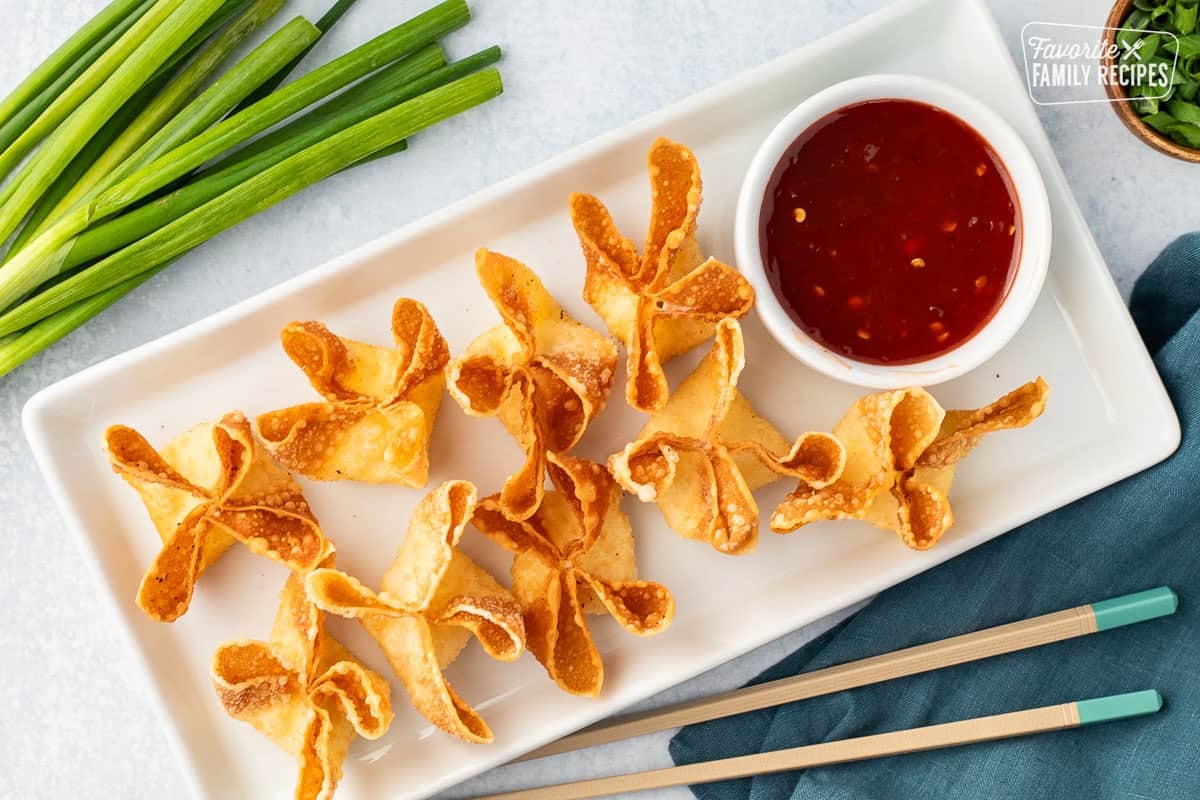 Cream cheese wontons on a platter next to a bowl of sweet-and-sour sauce.