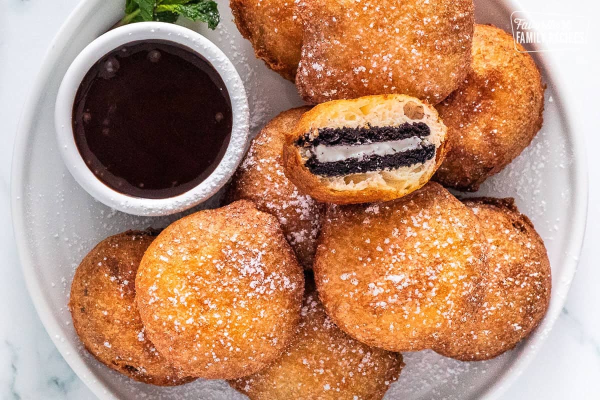 Plate of Deep fried Oreos with a bowl of chocolate sauce. One Oreo cut in half.