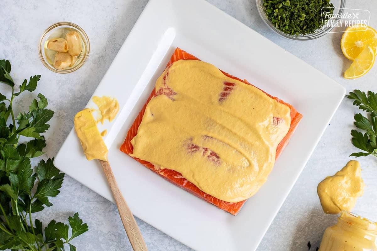 Salmon fillet with Dijon mustard spread on top with a spatula.