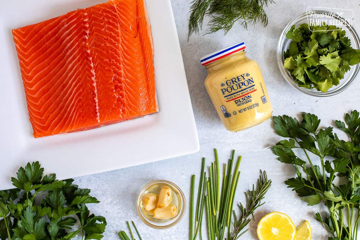 Ingredients to make herbed salmon including salmon, dill, cilantro, parsley, chives, rosemary, garlic, lemon and Dijon mustard.