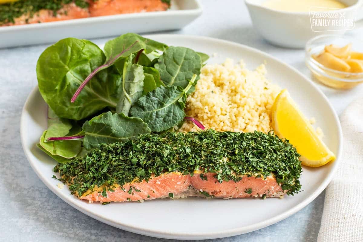 Slice of herbed salmon on a plate with fresh leaf lettuce and couscous.