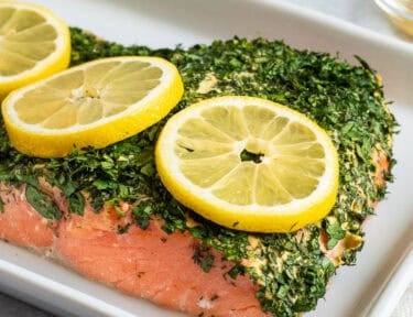Baked Herbed Salmon on a platter with slices of lemon garnish.