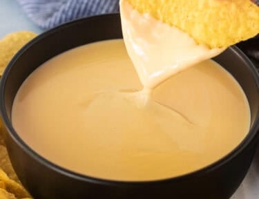 Dipping a tortilla chip into a bowl of cheddar cheese sauce.
