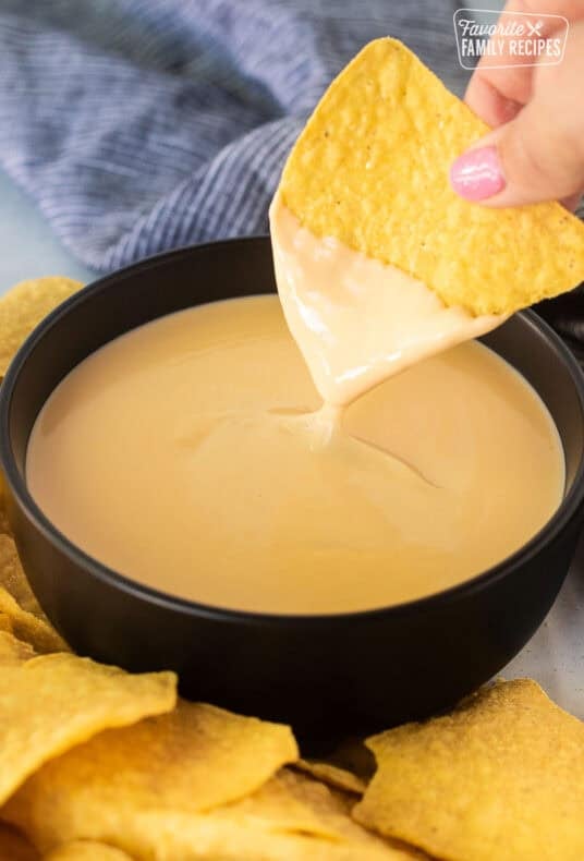 Dipping a tortilla chip into a bowl of cheddar cheese sauce.