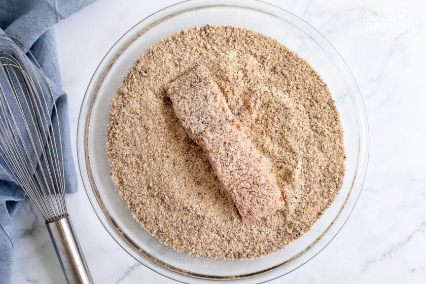 Piece of salmon coated with pecan mixture in a shallow glass dish.