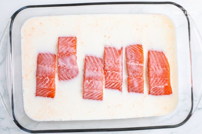 Glass baking dish with pieces of salmon and milk.